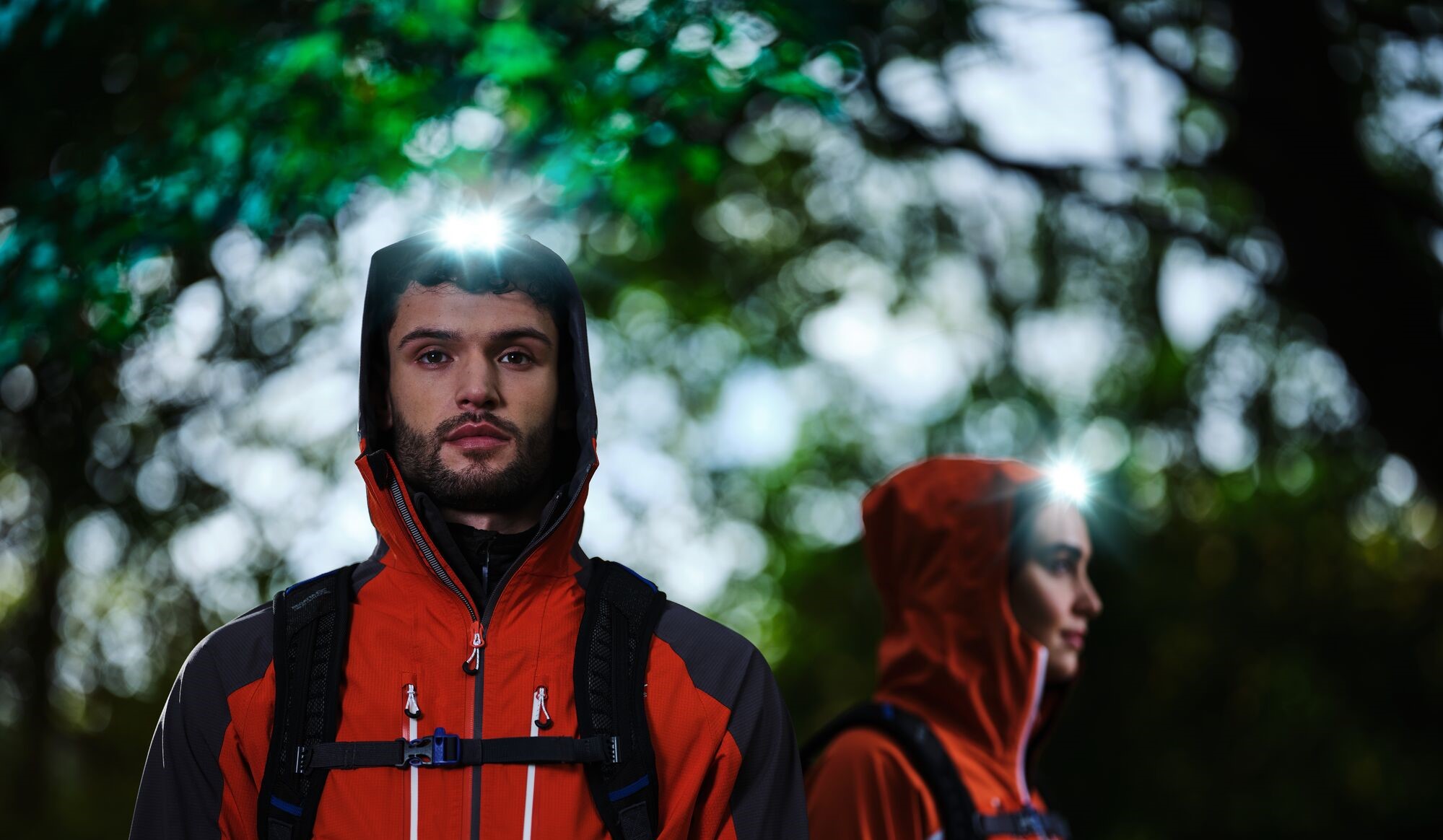 Man and woman wearing a red waterproof jacket with a head torch featured in the hood.